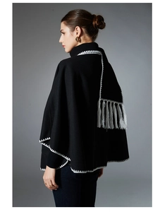 Detail of black knitted shawl featuring white wave embroidery and long grey fringes