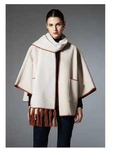 Detail of cream cape with brown zigzag embroidery and fringe hem on wool blend fabric
