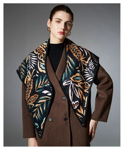 Detail view of jacquard leaf pattern scarf draped over a brown wool coat on model