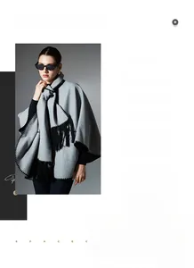 Detail of light grey knit shawl featuring black zigzag edges and long fringe tassels