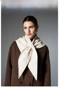 Detailed view of a soft beige winter triangle scarf knotted over a brown wool coat