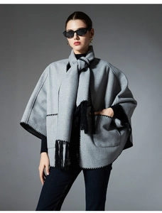 Detail of grey wool-textured poncho cape with black wavy embroidery and tassel hem decor