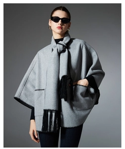 Detail of grey woolen poncho featuring handmade stitching, fringe hem, and cozy pockets