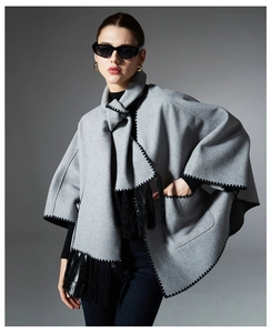 Close-up of grey poncho scarf showing black zigzag stitching, fringes and deep pocket detail
