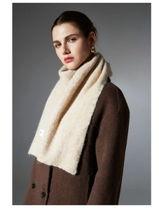 Detail of light beige knitted scarf featuring thick wool texture and a white sewn-on brand label