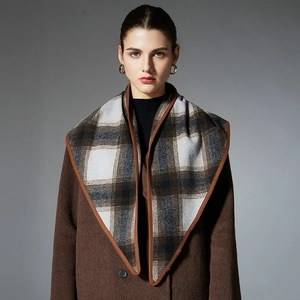 Women's plaid wool triangle scarf with fringe paired with a brown wool coat and golden earrings