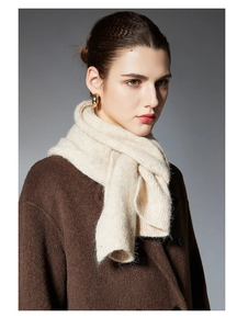 Close-up of beige chunky knit scarf paired with a brown wool coat and gold earrings