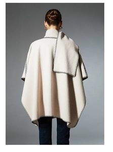 Detail of oat beige wool cape with black blanket stitch edges and integrated scarf style