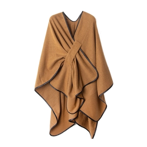 Elegant camel knit poncho featuring black leather trim and a stylish cross-collar design