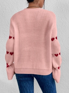 Détail d'un pull en tricot rose avec des motifs jacquard cœur rouge sur les manches