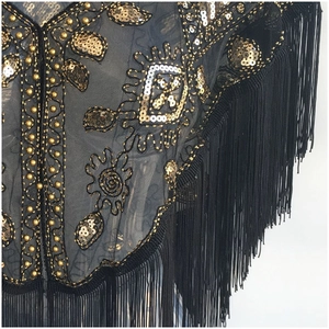 Macro detail of black mesh shawl with gold sequins, beads, and long fringe trim