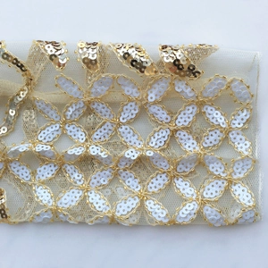 Detailansicht weißer Blumenpailletten und goldener Perlen auf dem Netzstoff der Bluse
