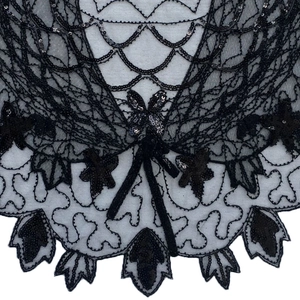 Détail de la cape en dentelle noire à paillettes avec broderie fine et nœud décoratif