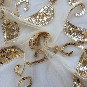 Detail of golden paisley sequins stitched on white tulle fabric for an evening shawl
