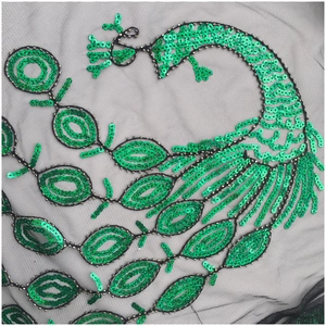 Détail de paillettes vert émeraude sur résille noire avec broderie en plumes de paon