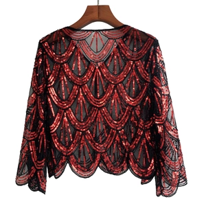 Detail of red sequins on black mesh shawl with wavy scale patterns and flared sleeves