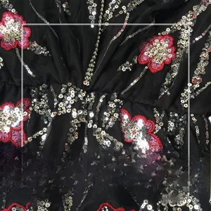 Détail de broderies florales et paillettes argentées sur tissu en maille noire pour robe