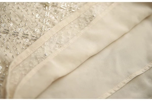 Détails de broderies pailletées argentées et perles sur un tissu mousseline champagne