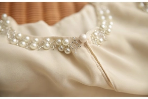 Détail de la broderie de perles et du bouton perle sur l'encolure en mousseline
