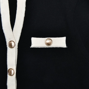 Close-up of black knit cardigan featuring cream ribbed trim and gold metal buttons