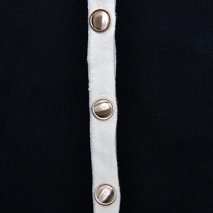 Detailed macro view of black knit fabric with white trim and gold metallic buttons