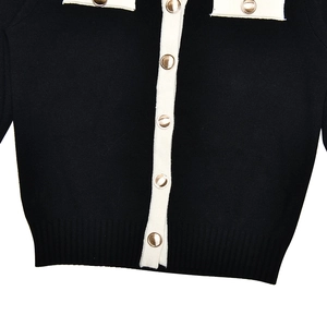 Detail shot of black knit cardigan with white trim and golden metal buttons