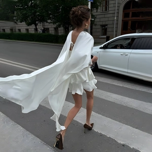 Détail de robe en satin blanc avec cape fluide et ourlet à volants étagés