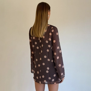 Détail d'une robe en mousseline marron foncé à grands pois roses avec des manches longues