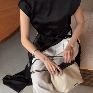 Dettaglio di un top in seta nera senza maniche con cintura intrecciata e pantaloni bianchi