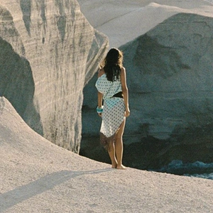 Detail of white polka dot beach cover-up with asymmetric one-shoulder design on a rocky coast