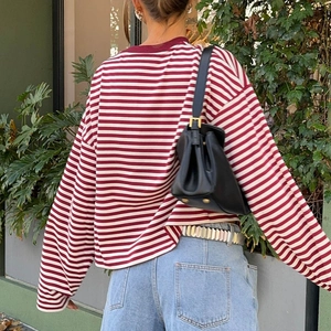 Outdoor back view of a woman wearing a red and white striped long-sleeve tee with denim jeans