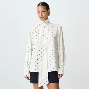 Detailed view of white polka dot blouse featuring an elegant tie-neck and buttoned cuffs