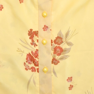 Close-up of vintage floral chiffon fabric with glossy yellow buttons on a light dress