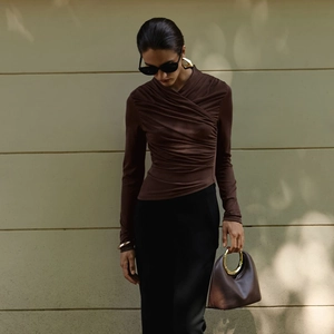 Detail of slim fit brown long sleeve top with irregular pleated hem and metal handle bag