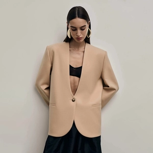 Detail of apricot blazer showing structured shoulders and metallic gold earrings on a model