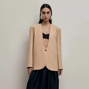 Detail of beige collarless blazer featuring a deep V-neck and a single gold button closure
