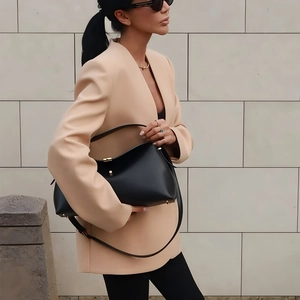 Detail of elegant black leather handbag with gold hardware worn with a beige blazer
