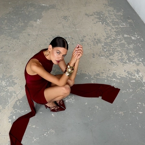 Détail de la robe moulante bordeaux sans manches avec longs rubans et bracelets dorés rigides