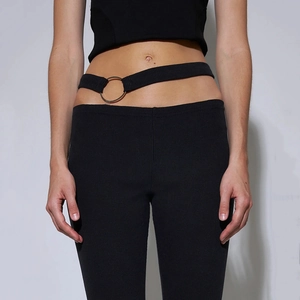 Close-up of black ribbed trousers featuring waist cutout and silver metal ring detail