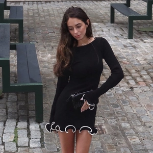 Detail of white wavy ruffle trim on the cuffs and hem of a black slim-fit knitted mini dress