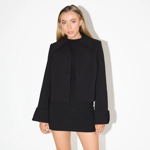 Close-up of a women's minimalist black cropped jacket and matching mini skirt on a model