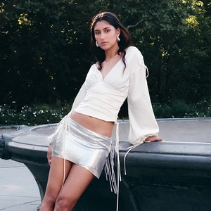 Détail du haut en satin blanc à lacets et de la jupe argentée à franges métalliques