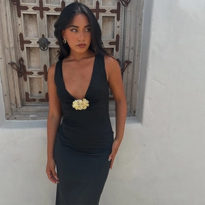 Détail d'une robe noire col en V avec une grande fleur dorée tridimensionnelle décorative