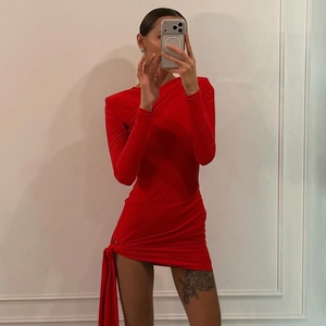 Detail of red long sleeve mini dress featuring side ribbon tie and ruched knit texture