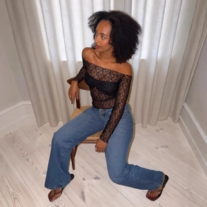 Detail of sheer black floral lace off-shoulder long sleeve top with intricate crochet texture