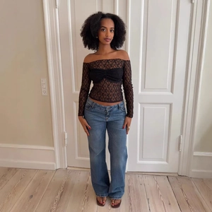 Detail of a slim fit black lace off-shoulder top with bow and blue wide leg jeans