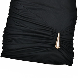 Détail d'une robe noire plissée ornée d'un accessoire métallique doré en forme de goutte