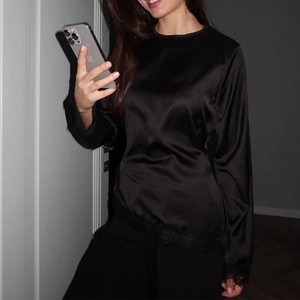 Close-up of elegant black satin top featuring delicate eyelash lace trim on sleeves and hem
