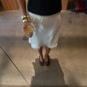 Dettaglio gonna in raso bianco a pois con pizzo e scarpe Tabi in pelle marrone