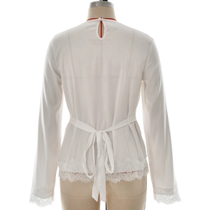 Detail of white long sleeve top featuring lace hem trim and back waist tie bow
